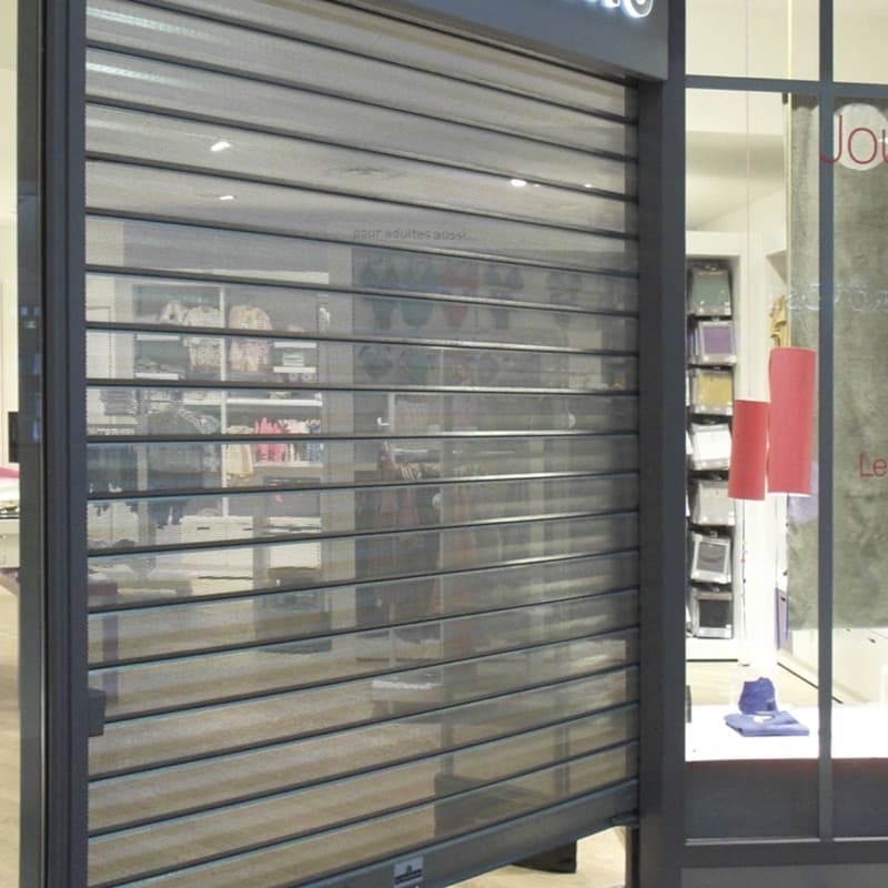 Rideau métallique à lames micro-perforées baissé devant une boutique : l’intérieur reste visible à travers le tablier